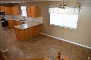 Kitchen with appliances with stainless steel finishes, sink, light stone counters, kitchen peninsula, and tasteful backsplash