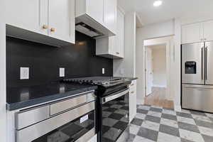 Kitchen featuring white cabinets, appliances with stainless steel finishes, wall chimney range hood, and tasteful backsplash