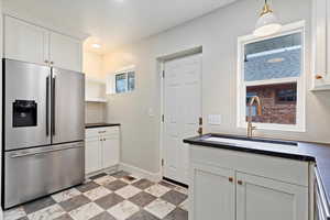 Kitchen with hanging light fixtures, stainless steel fridge, sink, dishwasher, and white cabinets