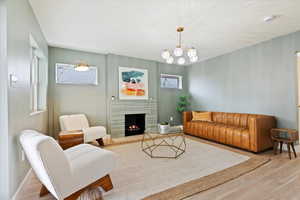 Living room with a notable chandelier, light wood-type flooring, and a stone fireplace