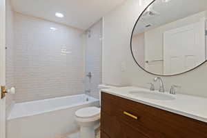 Full bathroom featuring tiled shower / bath combo, vanity, toilet, and a textured ceiling