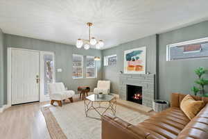 Living room with a notable chandelier, light hardwood / wood-style flooring, a stone fireplace, and a textured ceiling