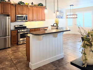 Kitchen featuring stainless steel appliances, lofted ceiling, decorative light fixtures, a kitchen bar, and a kitchen island with sink