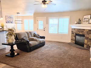 Carpeted living room featuring ceiling fan and a stone fireplace