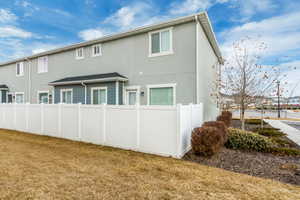 Rear view of house featuring fence, a lawn, and stucco siding