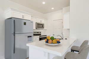 Kitchen with kitchen peninsula, sink, appliances with stainless steel finishes, white cabinets, and a breakfast bar area