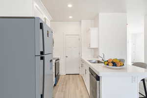 Kitchen with a breakfast bar, sink, light hardwood / wood-style floors, stainless steel appliances, and white cabinets