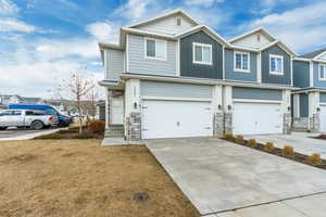 View of front of home with concrete driveway, board and batten siding, a garage, stone siding, and a front lawn