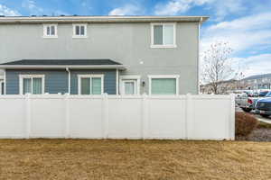 Back of house with stucco siding, fence, and a lawn