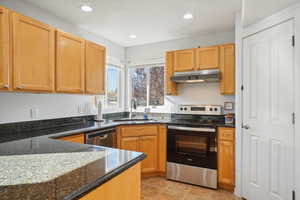 Kitchen with sink, appliances with stainless steel finishes, dark stone counters, and light tile patterned floors