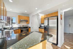 Kitchen with sink, dark stone counters, light hardwood / wood-style floors, stainless steel appliances, and kitchen peninsula