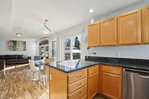 Kitchen with light wood-type flooring, dark stone counters, stainless steel dishwasher, and kitchen peninsula