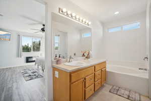 Bathroom with a wealth of natural light, wood-type flooring, vanity, and a relaxing tiled tub