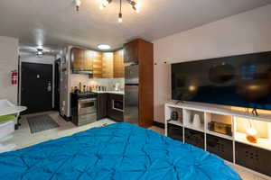 Bedroom with stainless steel refrigerator and a textured ceiling