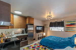 Tiled bedroom with stainless steel refrigerator, a wall unit AC, sink, and a textured ceiling