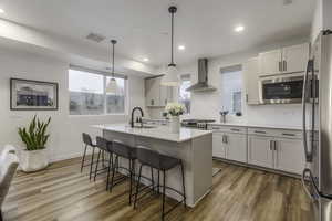 Kitchen with sink, pendant lighting, wall chimney range hood, black microwave, and an island with sink