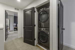 Washroom featuring stacked washing maching and dryer and light carpet