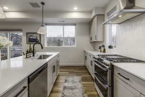 Kitchen featuring appliances with stainless steel finishes, hanging light fixtures, white cabinets, wall chimney range hood, and sink