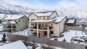 Snow covered back of property with a mountain view and a balcony