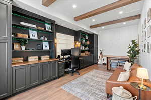 Home office featuring beamed ceiling, built in desk, and light hardwood / wood-style floors