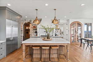 Kitchen with a spacious island, decorative light fixtures, stainless steel built in refrigerator, and gray cabinets