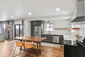 Kitchen with stainless steel appliances, wall chimney range hood, light hardwood / wood-style floors, gray cabinets, and sink