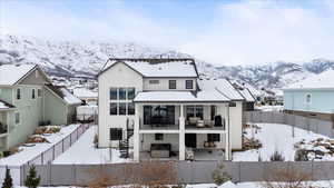 Snow covered back of property featuring a mountain view, central AC unit, and a balcony