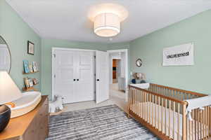 Bedroom with carpet floors, a closet, a textured ceiling, and a nursery area