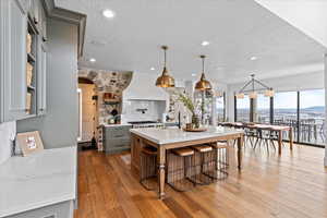 Kitchen featuring a center island with sink, gray cabinetry, decorative light fixtures, light hardwood / wood-style floors, and a breakfast bar