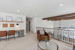 Office area featuring beamed ceiling, a textured ceiling, ceiling fan, built in desk, and light carpet