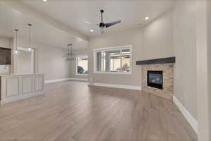 Unfurnished living room featuring sink, ceiling fan, a stone fireplace, and light hardwood / wood-style floors