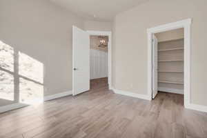 Unfurnished bedroom featuring light wood-type flooring, an inviting chandelier, a spacious closet, and a closet