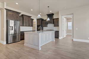 Kitchen with backsplash, custom range hood, decorative light fixtures, stainless steel appliances, and an island with sink