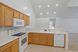 Kitchen with sink, white appliances, light brown cabinetry, light carpet, and kitchen peninsula