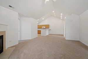 Unfurnished living room with ceiling fan, light colored carpet, a fireplace, and high vaulted ceiling