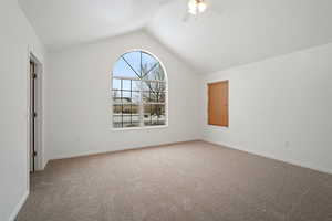 Carpeted spare room featuring lofted ceiling and ceiling fan