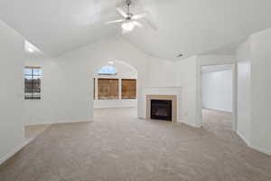 Unfurnished living room featuring light carpet, vaulted ceiling, and a healthy amount of sunlight