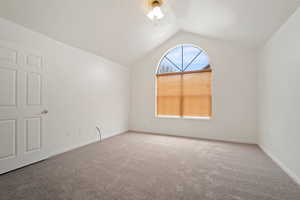 Carpeted spare room featuring vaulted ceiling