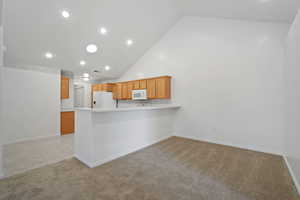 Kitchen featuring light carpet, white appliances, high vaulted ceiling, and kitchen peninsula