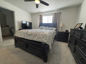 Carpeted bedroom featuring ceiling fan, ensuite bath, and a textured ceiling