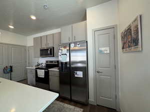 Kitchen with tasteful backsplash, appliances with stainless steel finishes, dark wood-type flooring, and a textured ceiling