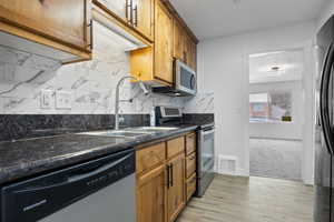 Kitchen featuring dark stone countertops, light hardwood / wood-style flooring, sink, appliances with stainless steel finishes, and decorative backsplash