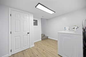 Laundry room with electric panel, light hardwood / wood-style flooring, and washing machine and clothes dryer