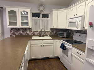 Kitchen featuring white appliances, sink, dark wood-type flooring, white cabinets, and tasteful backsplash