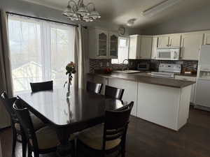 Kitchen featuring lofted ceiling, hanging light fixtures, sink, white appliances, and white cabinets