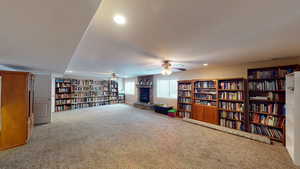 Living area featuring a large fireplace, carpet flooring, a textured ceiling, and ceiling fan