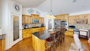 Kitchen featuring an island with sink, stainless steel appliances, decorative light fixtures, sink, and dark stone countertops