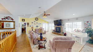 Living room featuring a fireplace, ceiling fan, vaulted ceiling, and a healthy amount of sunlight