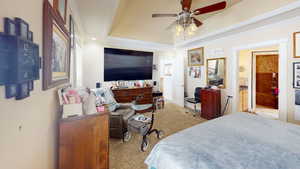 Bedroom featuring ensuite bath, a tray ceiling, crown molding, ceiling fan, and light colored carpet