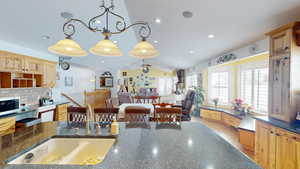 Kitchen with lofted ceiling, hanging light fixtures, sink, backsplash, and dark stone counters